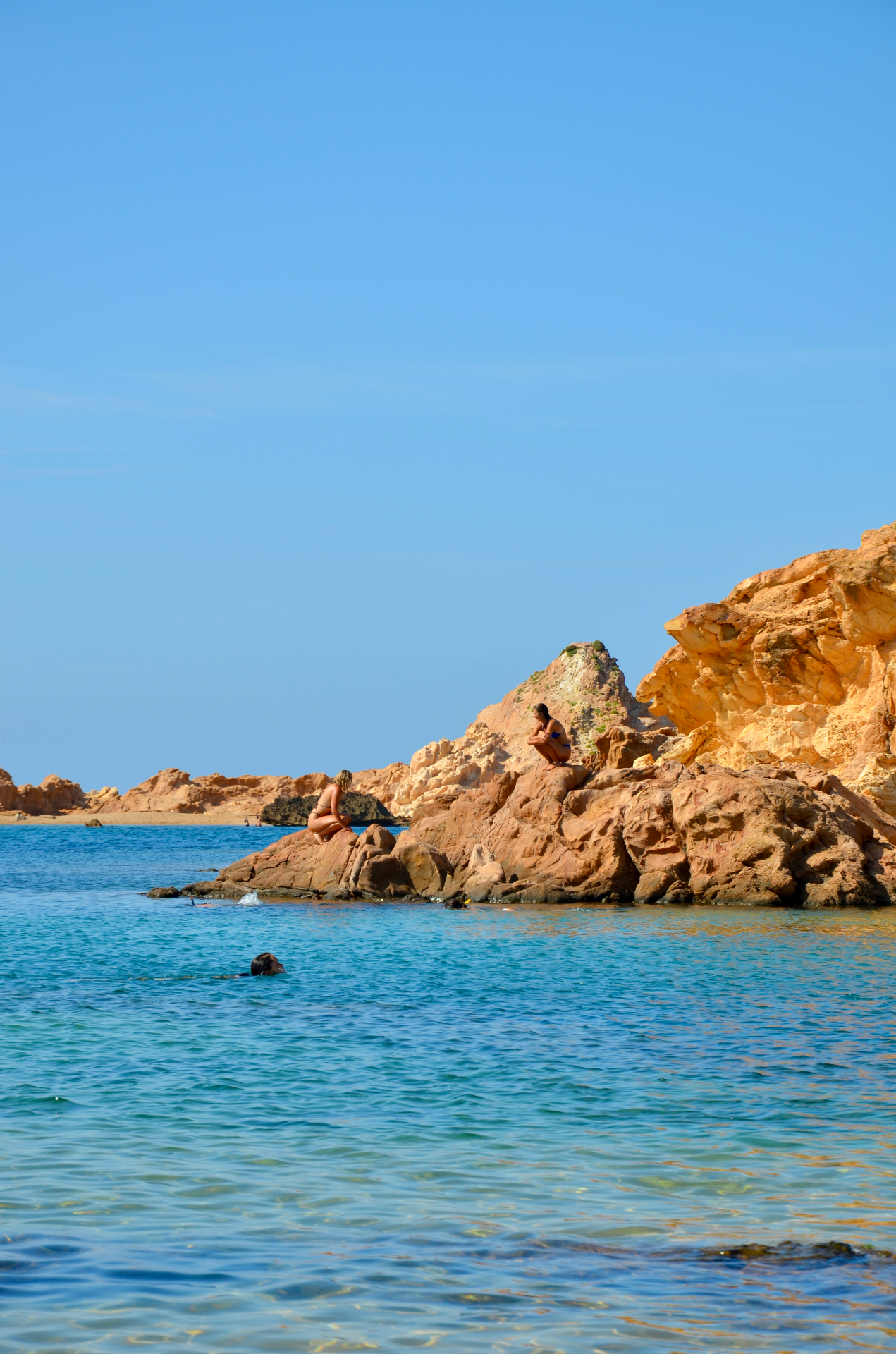 Swimmers in a turquoise Mediterranean cove framed by golden cliffs